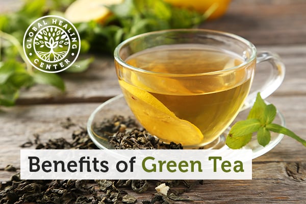 Cup of green tea with leaves around it. Green tea possesses great benefits for your health.