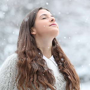 A woman taking a deep breath in a cold environment surrounded by falling snowflakes.
