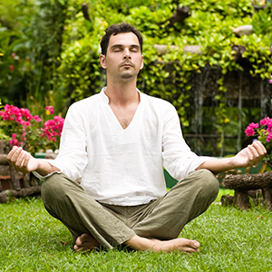 A meditating man sitting in an open green space with eyes closed.